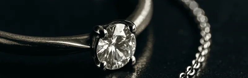 Schmuckfotografie im Studio: Goldring mit funkelndem Diamant und Silberkette auf dunklem Untergrund, reflexionskontrolliert ausgeleuchtet