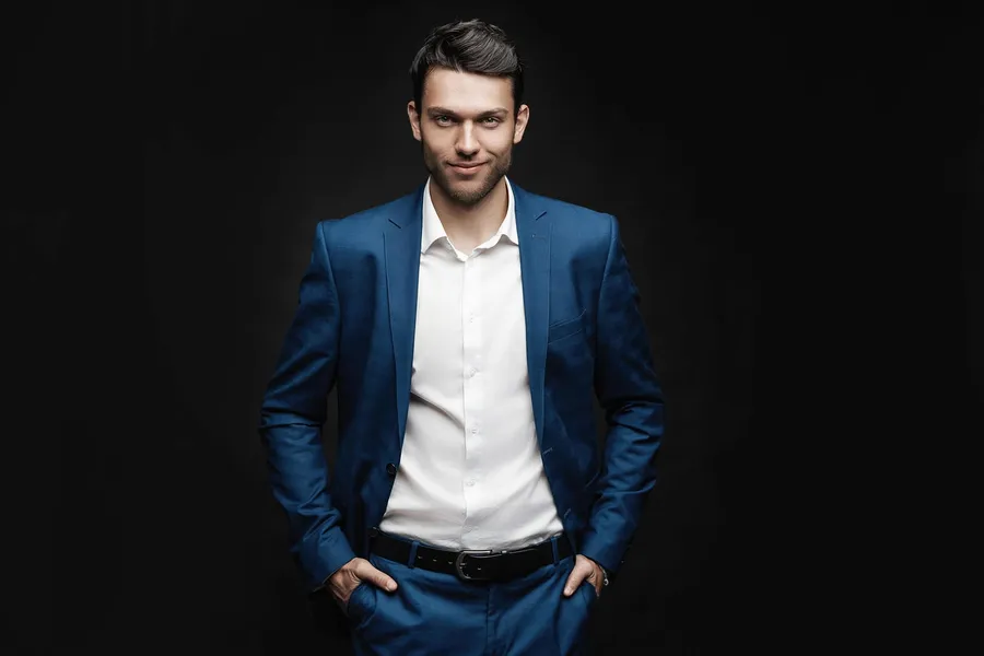 Ein junger Mann im blauen Anzug posiert vor schwarzem Hintergrund.