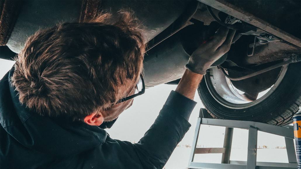 Ein Mann macht Industriefotografie, während er an der Unterseite eines Autos arbeitet.