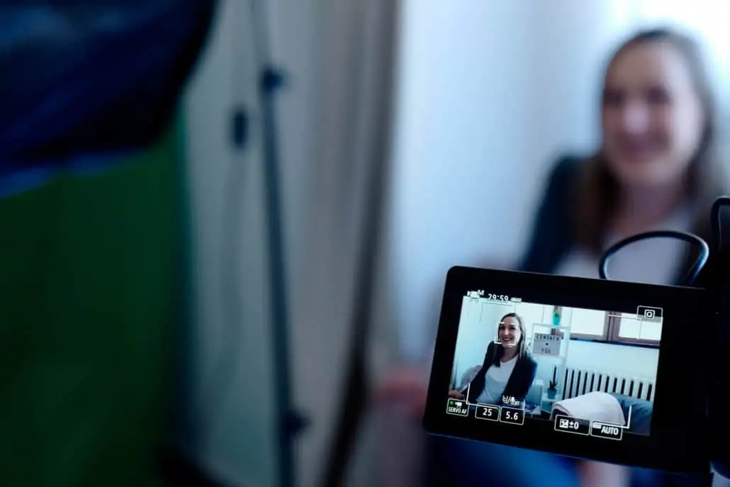 Eine Frau hält eine Videokamera vor eine Kamera.