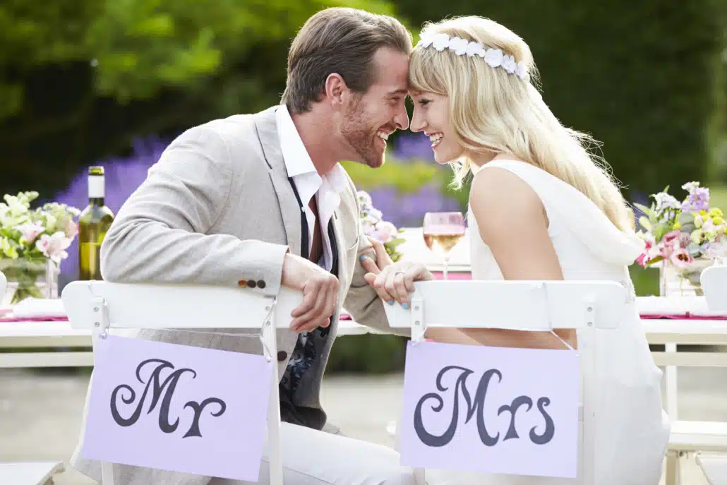 Eine Braut und ein Bräutigam sitzen an einem Tisch mit Herrn- und Frau-Schildern.