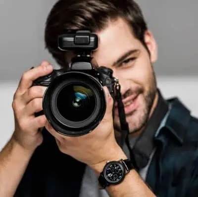 photo-smiling-young-man-photographing-camera-studolehner Professioneller Fotograf in Aktion mit DSLR-Kamera
